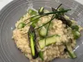 Kremowe risotto z zielonymi szparagami i szczypiorkiem na szarym talerzu.