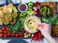 Taca z przekąskami na ognisko: hummus, falafel, warzywa, owoce, pieczywo i paluszki.