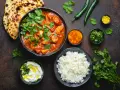 Curry z kurczakiem, ryż, chlebki naan, jogurt i przyprawy na ciemnym tle.
