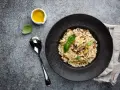 Kremowe risotto z grzybami na czarnym talerzu, obok łyżka i oliwa.