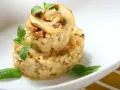 Kremowe risotto z grzybami i ziołami, udekorowane plasterkami pieczarek i listkami bazylii.