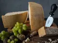 Kawałki parmezanu, winogrona i orzechy na drewnianych deskach. Widać wyraźne tłoczenia na skórce, które pokazują, jak wygląda parmezan.