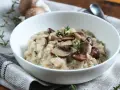 Kremowe risotto z pieczarkami i świeżym tymiankiem w białej misce.