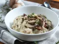 Kremowe risotto z pieczarkami i serem pleśniowym, udekorowane świeżym tymiankiem.