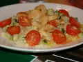 Risotto z krewetkami i pomidorkami koktajlowymi na białym talerzu.