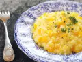 Kremowe risotto z dynią na talerzu z niebieskimi wzorami, obok widelca.