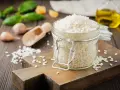 Słoik z ryżem do risotto, drewniana deska, czosnek, bazylia i oliwa.