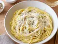 Miseczka spaghetti posypana parmezanem i pieprzem, obok przyprawy i czosnek.