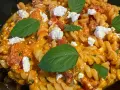Makaron fusilli w pomarańczowym sosie z kawałkami sera i listkami bazylii.
