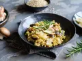 Miseczka risotto z grzybami i parmezanem, udekorowana rozmarynem.