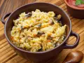 Kremowe risotto z grzybami i marchewką w brązowej misce, obok drewniana łyżka.