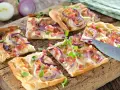 Kawałki pizzy z cebulą i boczkiem na drewnianej desce.