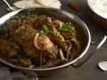 Kurczak w sosie garam masala z cebulą i kolendrą w metalowej misie.