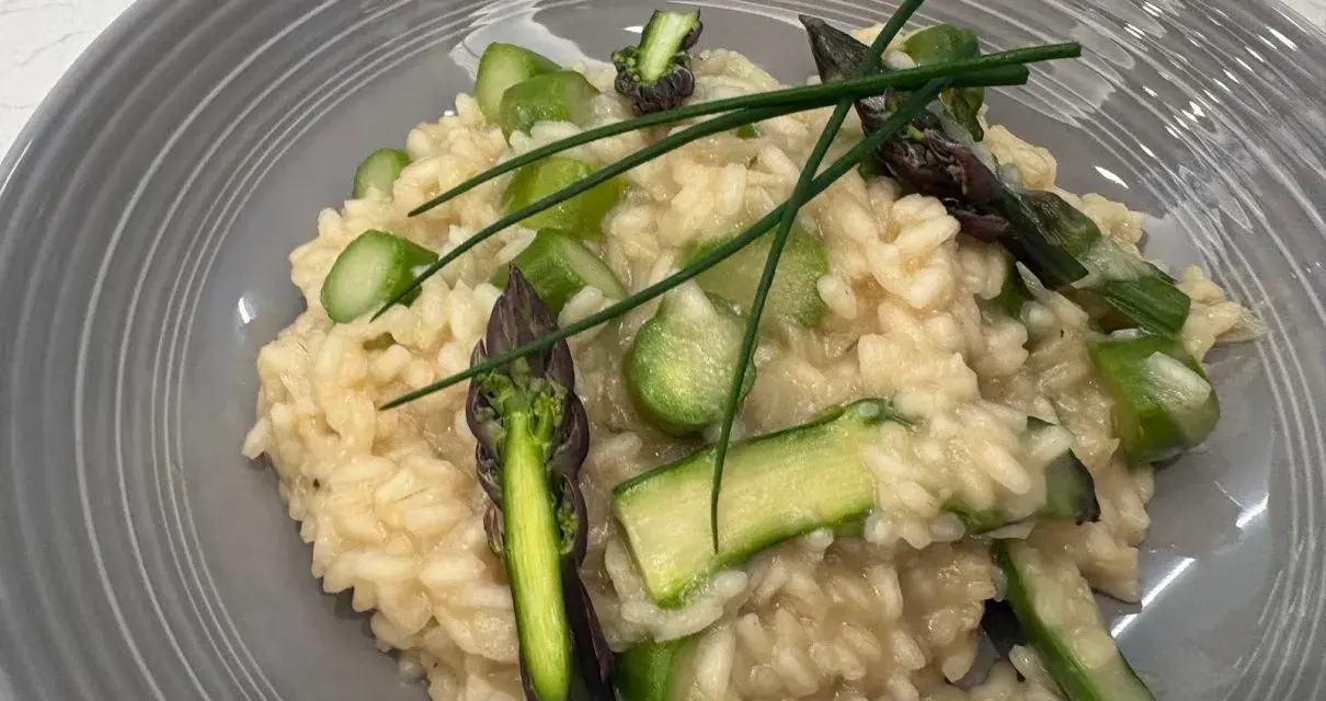 Kremowe risotto z zielonymi szparagami i szczypiorkiem na szarym talerzu.