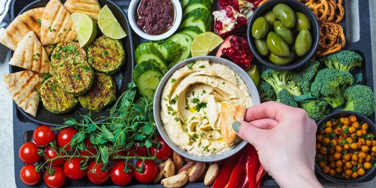 Taca z przekąskami na ognisko: hummus, falafel, warzywa, owoce, pieczywo i paluszki.
