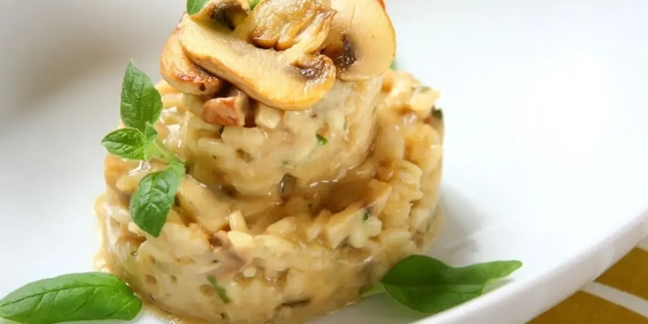 Kremowe risotto z grzybami i ziołami, udekorowane plasterkami pieczarek i listkami bazylii.