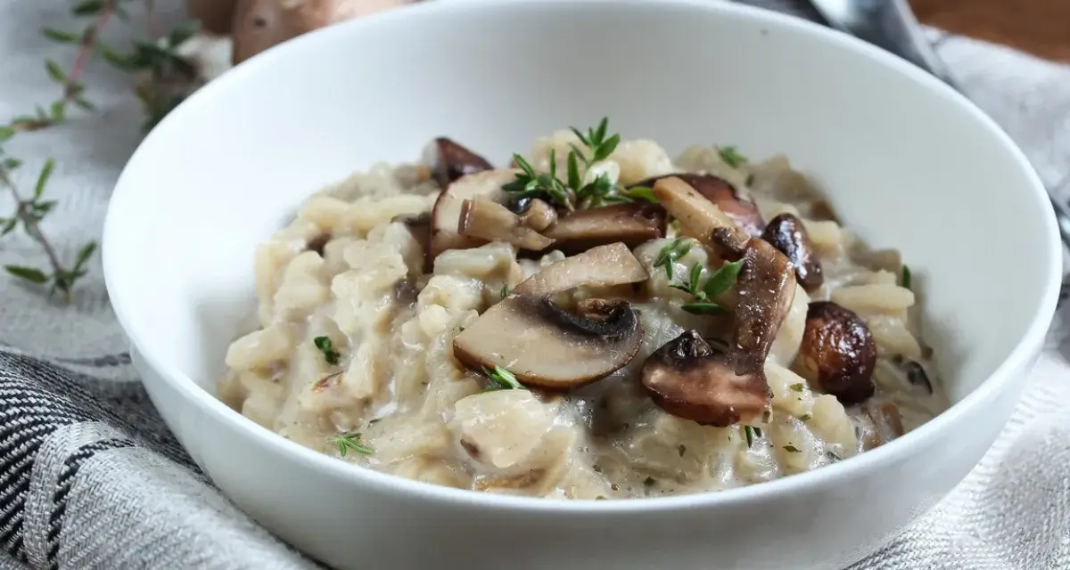 Kremowe risotto z pieczarkami i świeżym tymiankiem w białej misce.