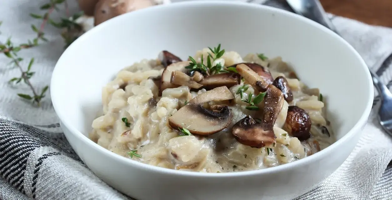 Kremowe risotto z pieczarkami i serem pleśniowym, udekorowane świeżym tymiankiem.