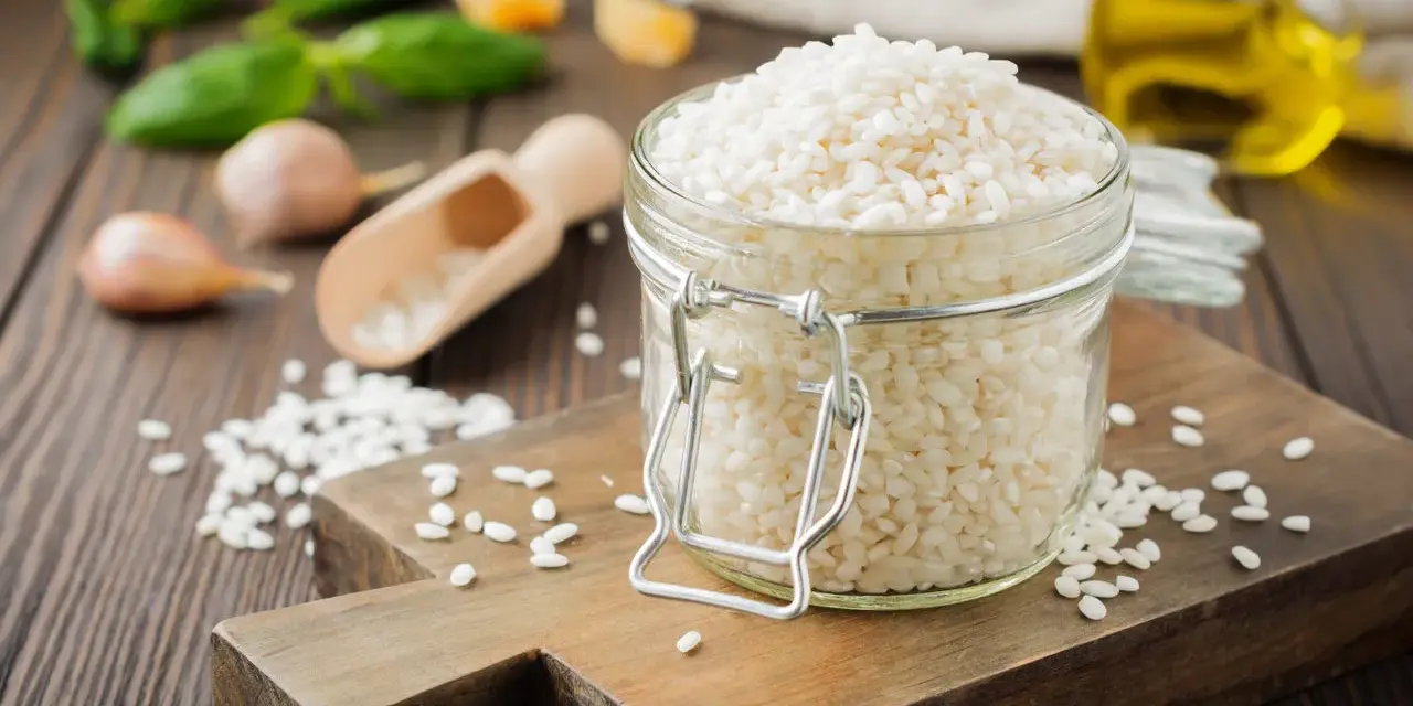 Słoik z ryżem do risotto, drewniana deska, czosnek, bazylia i oliwa.