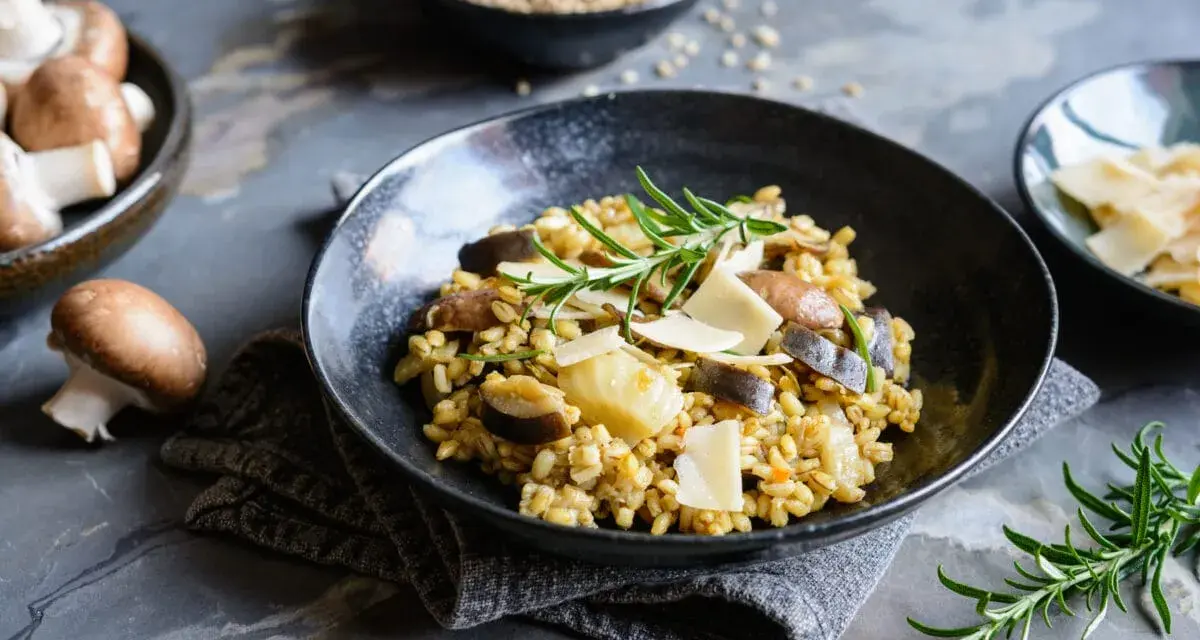Miseczka risotto z grzybami i parmezanem, udekorowana rozmarynem.