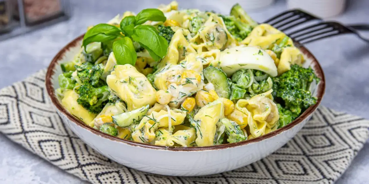Sałatka z tortellini, brokułów, kukurydzy i jajka w kremowym sosie, udekorowana bazylią.