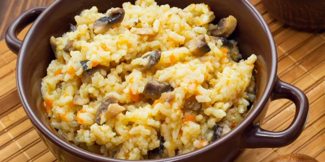 Kremowe risotto z grzybami i marchewką w brązowej misce, obok drewniana łyżka.