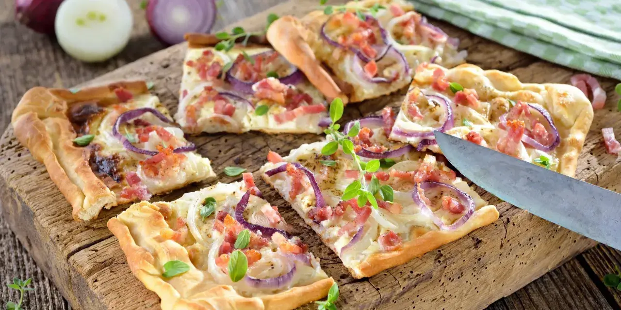 Kawałki pizzy z cebulą i boczkiem na drewnianej desce.