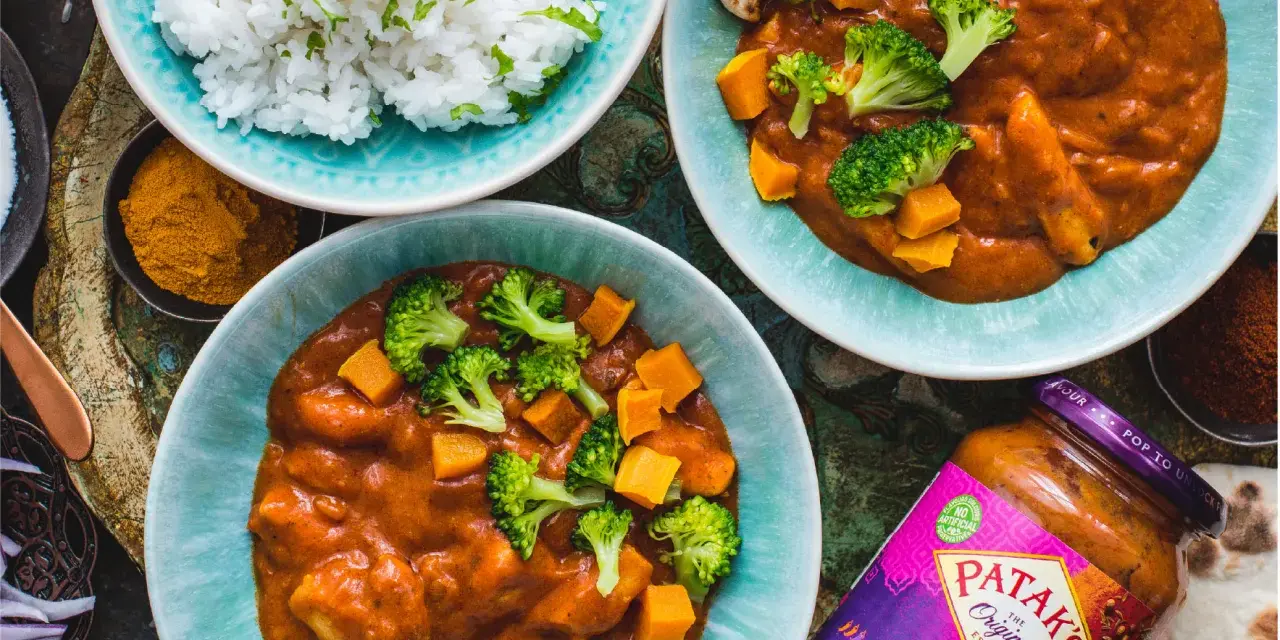 Dwa talerze z sosem Tikka Masala, ryżem, brokułami i dynią, obok słoik sosu.