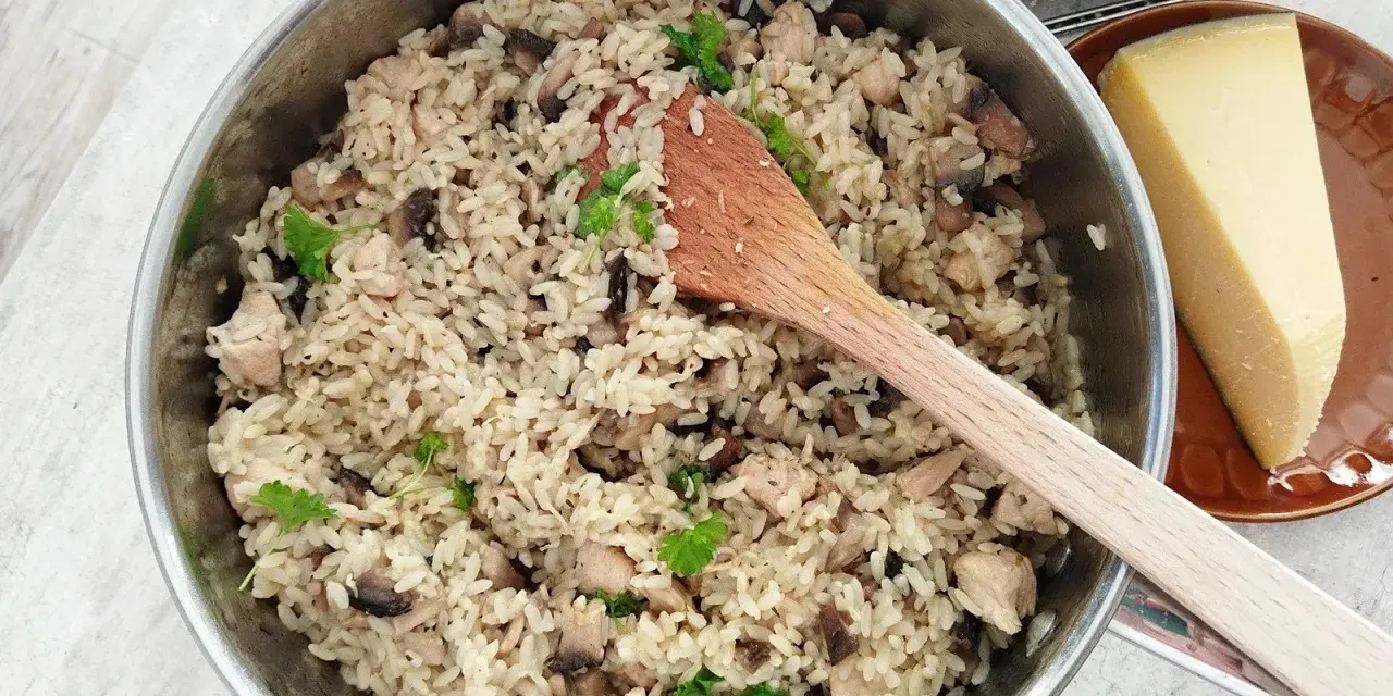 Kremowe risotto z pieczarkami i kurczakiem w garnku, obok kawałek parmezanu i tarka.