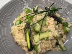 Kremowe risotto z zielonymi szparagami i szczypiorkiem na szarym talerzu.