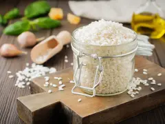 Słoik z ryżem do risotto, drewniana deska, czosnek, bazylia i oliwa.