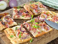 Kawałki pizzy z cebulą i boczkiem na drewnianej desce.
