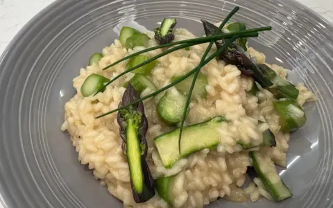 Kremowe risotto z zielonymi szparagami i szczypiorkiem na szarym talerzu.