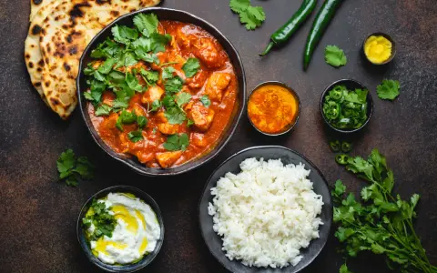 Curry z kurczakiem, ryż, chlebki naan, jogurt i przyprawy na ciemnym tle.