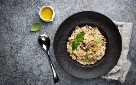Kremowe risotto z grzybami na czarnym talerzu, obok łyżka i oliwa.