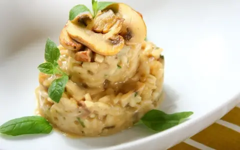 Kremowe risotto z grzybami i ziołami, udekorowane plasterkami pieczarek i listkami bazylii.