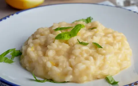 Kremowe risotto cytrynowe z bazylią na talerzu, w tle połówka cytryny.