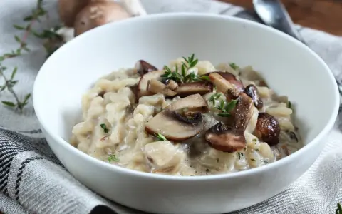 Kremowe risotto z pieczarkami i świeżym tymiankiem w białej misce.
