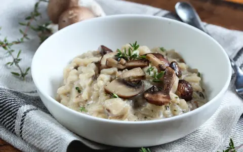 Kremowe risotto z pieczarkami i serem pleśniowym, udekorowane świeżym tymiankiem.