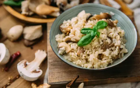 Miseczka kremowego risotto z grzybami i bazylią, otoczona świeżymi grzybami i przyprawami.