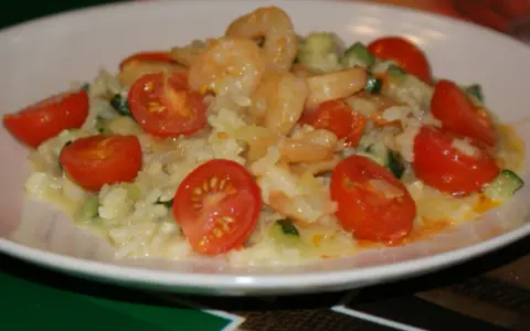 Risotto z krewetkami i pomidorkami koktajlowymi na białym talerzu.