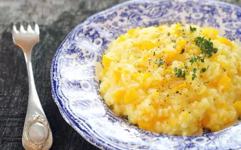 Kremowe risotto z dynią na talerzu z niebieskimi wzorami, obok widelca.