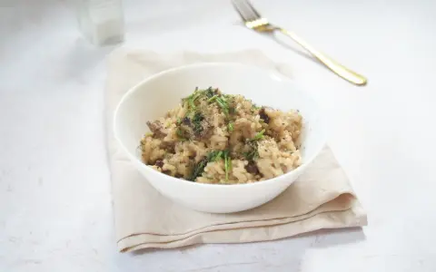 Miseczka kremowego risotto z grzybami, posypana ziołami i pieprzem, obok złoty widelec.