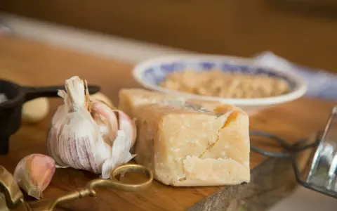 Kawałek parmezanu, czosnek i tarka na drewnianej desce.