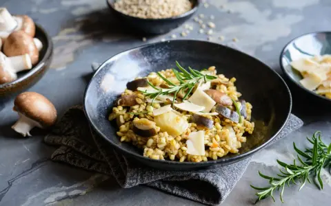 Miseczka risotto z grzybami i parmezanem, udekorowana rozmarynem.