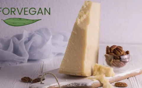 Kawałek sera parmezan, orzechy pekan w szklanej miseczce i liść z napisem FORVEGAN.