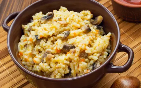 Kremowe risotto z grzybami i marchewką w brązowej misce, obok drewniana łyżka.