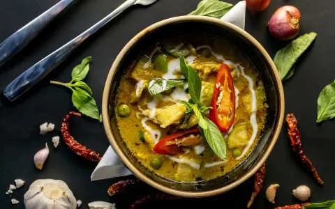 Zielone curry w misce, ozdobione chili i bazylią, otoczone przyprawami.