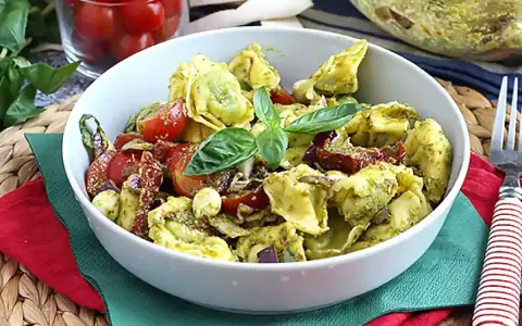 Miseczka tortellini z pesto, pomidorkami koktajlowymi i bazylią.
