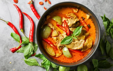 Miseczka czerwonego curry z mięsem, warzywami, papryczkami chili i bazylią.